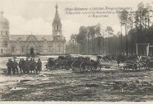 Zdjęcie czarno- białe z początku XX wieku ukazujące centrum Augustowa podczas I Wojny Światowej,na tle cerkwi po lewej stronie stoi grupa dziewięciu żołnierzy, pozująca do zdjęcia a po prawej stronie jest dużo armat.
