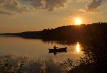 Zachód słońca nad Jeziorem Sajno,po którym płynie łódką wędkarz, fot. J. Koniecko
