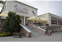 Zdjęcie przedstawia restaurację Albatros z zewnątrz, przd budynkiem widoczne schody, które prowadzą na piętro. Na piętrze po lewej stronie wioczne dwa rozłożone parasole. Po lewej stronie przed restauracją pomnij Beaty z Albatrosa. Na budynku duży neon z napisem: Albatros