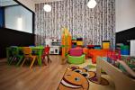 Zdjęcie przedstawia pokój animacyjny dla dzieci. Widać dużo zabawek takich jak piłki, klocki, pufy. Po lewej stronie kuchnia dla dzieci i mały stolik z niskimi kolorowymi krzesełkami. Na podłodze drewniane panela, na ścienie fototapeta imitująca brzozowe pnie