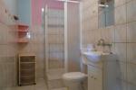 Zdjęcie przedstawia wnętrze łazienki. Na zdjęciu widać: toaletę, kabinę prysznicową, zlew, białą szafkę. Łazienka wykończana jest jasnobeżowymi płytkami 